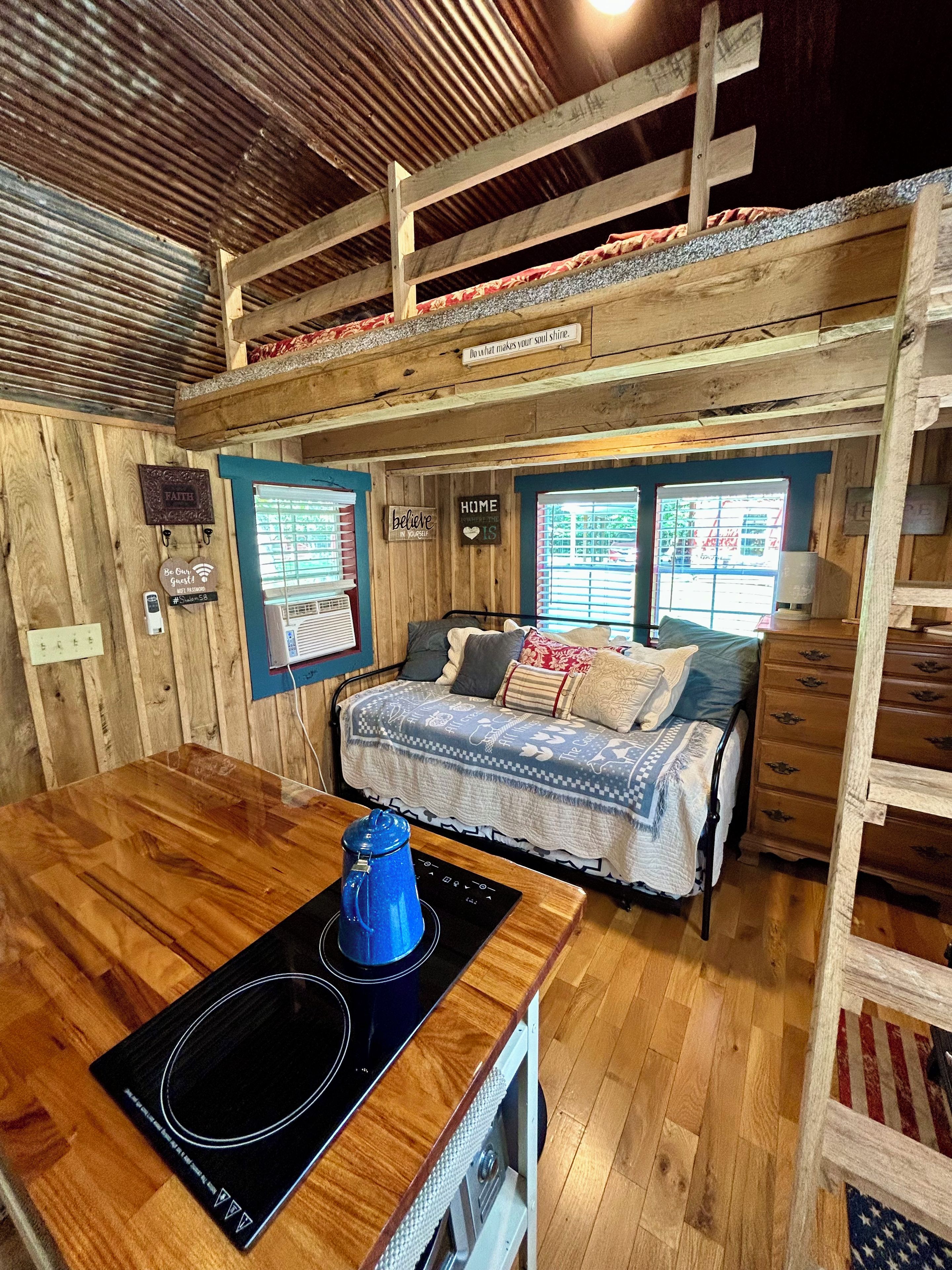 Ein gemütliches Blockhauszimmer mit einem Bett, einer kleinen Küchenzeile mit Induktionskochfeld und einer Holzbalkendecke.