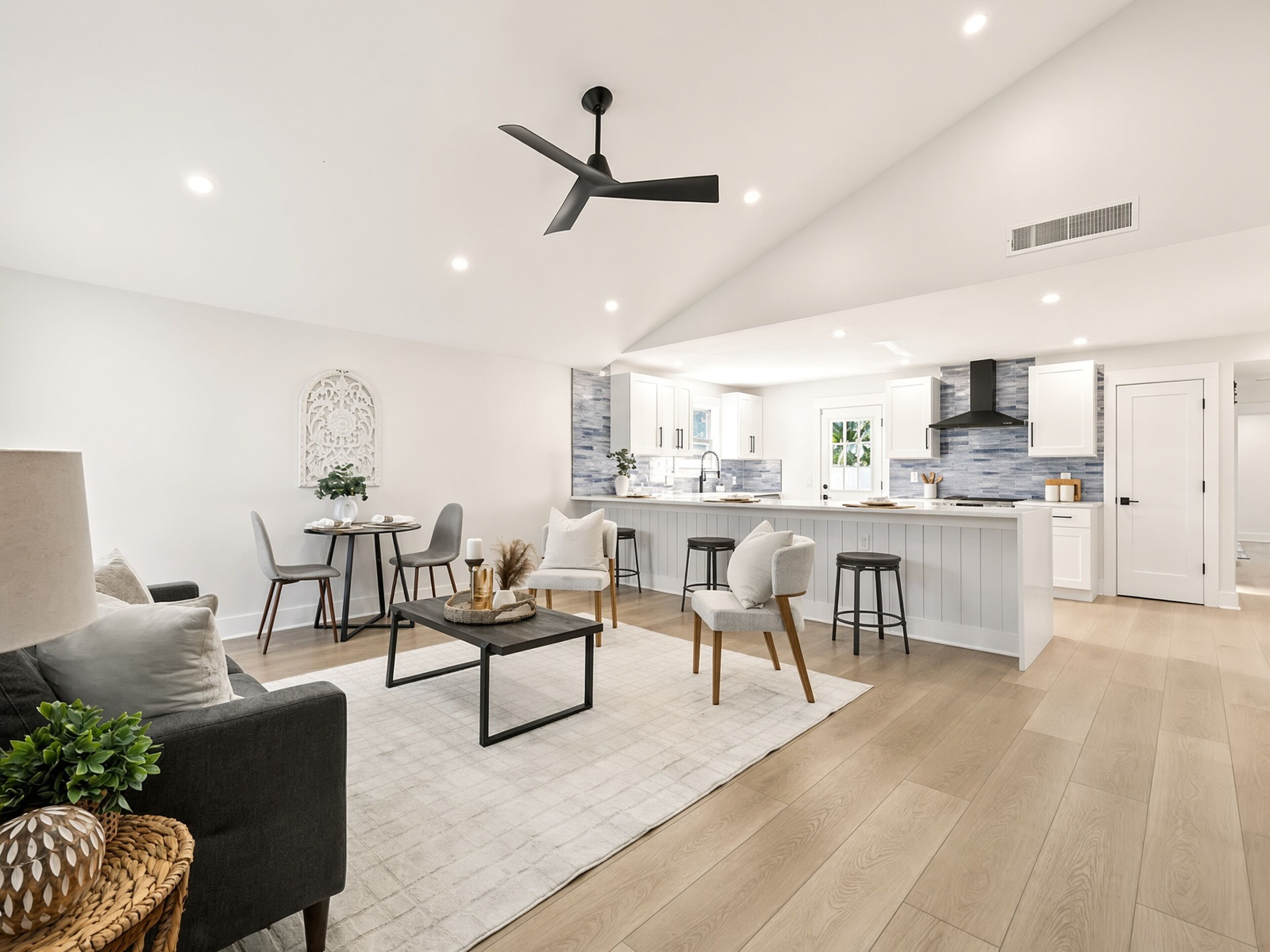 Una cocina moderna con armarios blancos, un ventilador de techo negro y una isla central con taburetes.