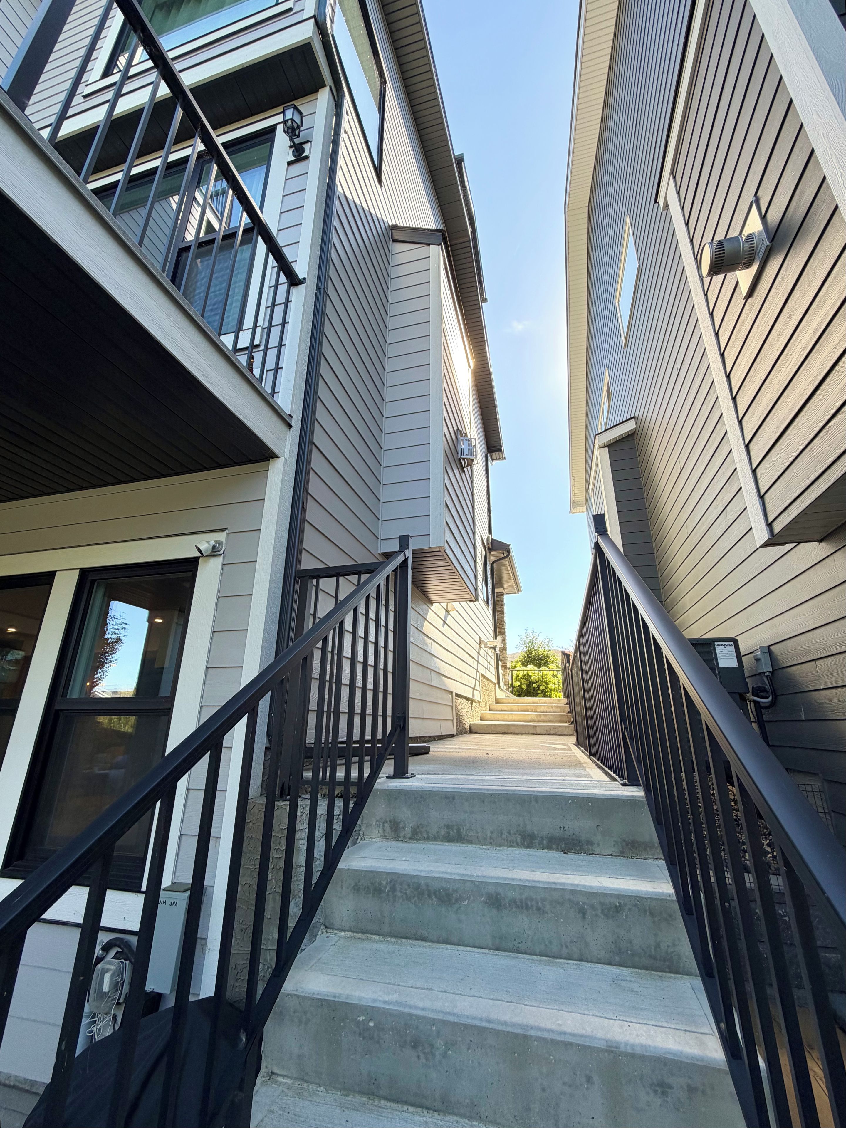 A staircase leading to a residential building with a modern design, featuring a metal railing and a clear sky above.