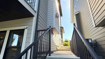 A staircase leading to a residential building with a modern design, featuring a metal railing and a clear sky above.