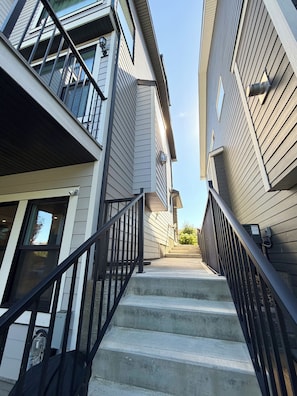 A staircase leading to a residential building with a modern design, featuring a metal railing and a clear sky above.