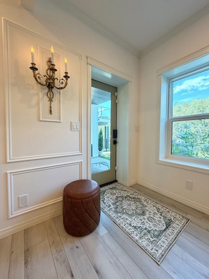 A hallway with a chandelier, a door leading outside, a window with a view, and a patterned rug. - Stay at a remarkable English chateau style with a view & full optional services. (Calgary)