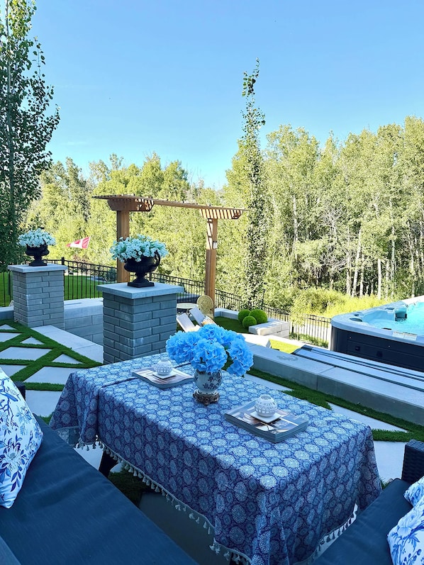 An outdoor patio with a table set for dining, surrounded by greenery and a hot tub.
