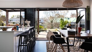 A modern kitchen with a bar area, large windows, and a view of the outdoors. - Fontaine - Stunning 4 bedroom (Daylesford)