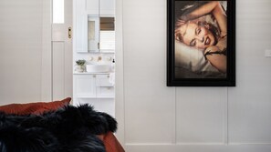 Une chambre à coucher avec un lit, un tableau encadré au mur, et une salle de bain avec un lavabo et un miroir.