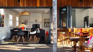 An open-plan living and dining area with a wooden ceiling, a dining table with chairs, a sofa, and a hanging light fixture. - Fontaine - Stunning 4 bedroom (Daylesford)