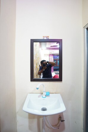 Un baño con un lavamanos blanco, un espejo y una persona tomando una fotografía.