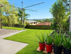 Ein Garten mit Rasen, einer Holzterrasse und Blumentöpfen.