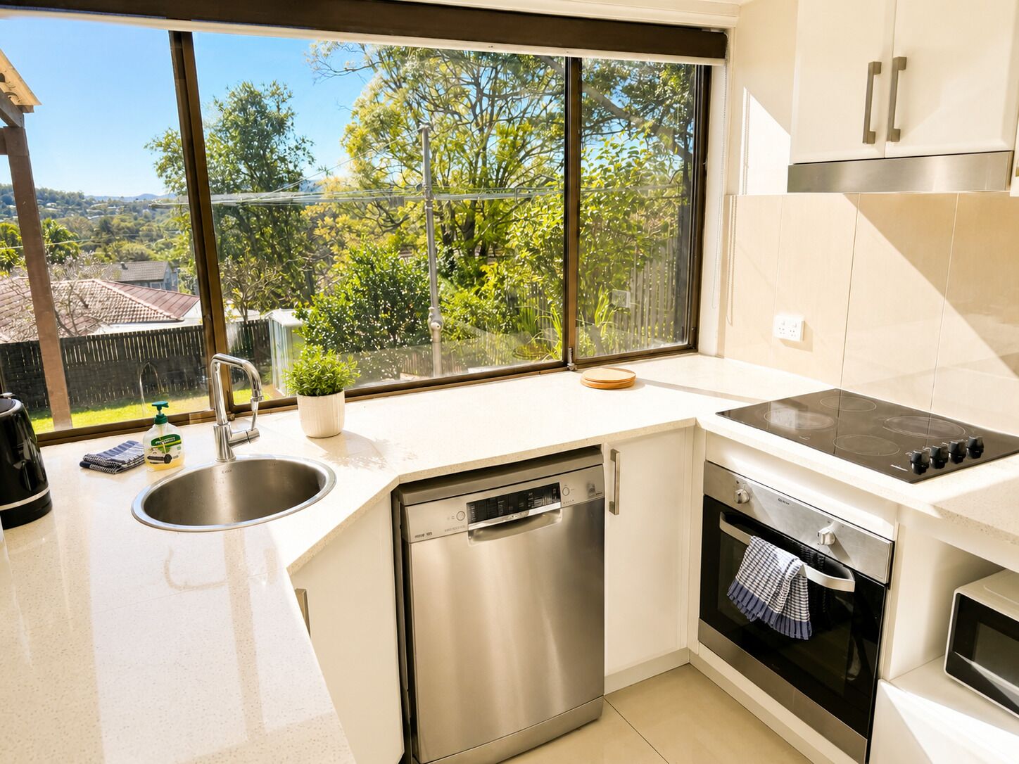 A modern kitchen with a dishwasher, oven, and a large window offering a view of greenery.
