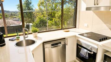 A modern kitchen with a dishwasher, oven, and a large window offering a view of greenery.