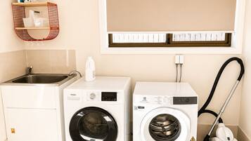 A compact laundry room with a washing machine, a dryer, and a vacuum cleaner.