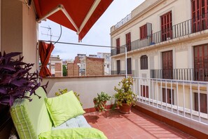 Ein Balkon mit rotem Sonnensegel, einem grün gestreiften Sofa und Topfpflanzen.