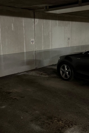 A parking garage with concrete walls, numbered parking spots, and a car parked in one of the spots. - Waldhaus Panorama Home (CharmingStay), (Flumserberg Tannenbodenalp), by Interhome (Flumserberg Tannenbodenalp)