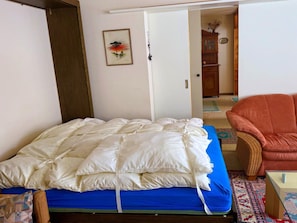 Ein Schlafzimmer mit einem Bett, einem Sessel und einer Tür zu einem anderen Raum.
