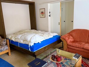 A bedroom with a single bed, a chair, a small table with a book, and a decorative plate. - Waldhaus Panorama Home (CharmingStay), (Flumserberg Tannenbodenalp), by Interhome (Flumserberg Tannenbodenalp)