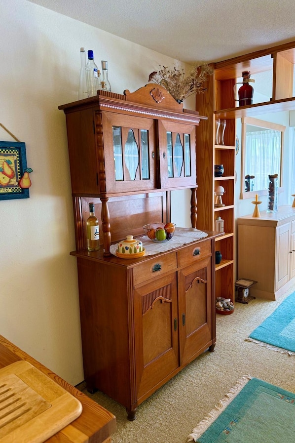 A wooden cabinet with glass doors, a small table with a vase, and a shelf with decorative items. - Waldhaus Panorama Home (CharmingStay), (Flumserberg Tannenbodenalp), by Interhome (Flumserberg Tannenbodenalp)