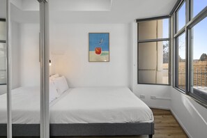 A bedroom with a bed, a painting, and large windows. - Stylish 2-Bed Apartment Near Melbourne Central (Carlton)