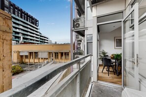 Ein Balkon mit Blick auf ein Gebäude, ein Essbereich mit Tisch und Stühlen sowie eine Tür zu einem Innenraum.