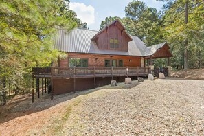 A cabin with a metal roof, wooden deck, and a gravel driveway. - Hot Tub, Cold Plunge, Pool Table & Veranda (Hochatown)