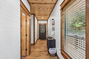 A hallway with wooden flooring, white walls, and a door at the end. - Hot Tub, Cold Plunge, Pool Table & Veranda (Hochatown)