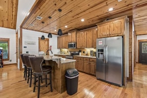 A kitchen with wooden cabinets, stainless steel appliances, and a bar area with stools. - Hot Tub, Cold Plunge, Pool Table & Veranda (Hochatown)