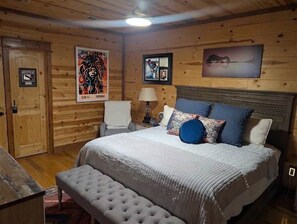 A wooden-paneled room with a bed, a bench, a nightstand, and a wall-mounted lamp. - Hot Tub, Cold Plunge, Pool Table & Veranda (Hochatown)