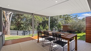 Eine Gartenpatio mit einem Holztisch und Stühlen, umgeben von einem Garten und einem Ziegelbau.