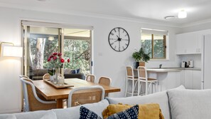 A modern living room with a dining area, white cabinetry, and a large wall clock. - Nazza Daze in Narawallee (Narrawallee)
