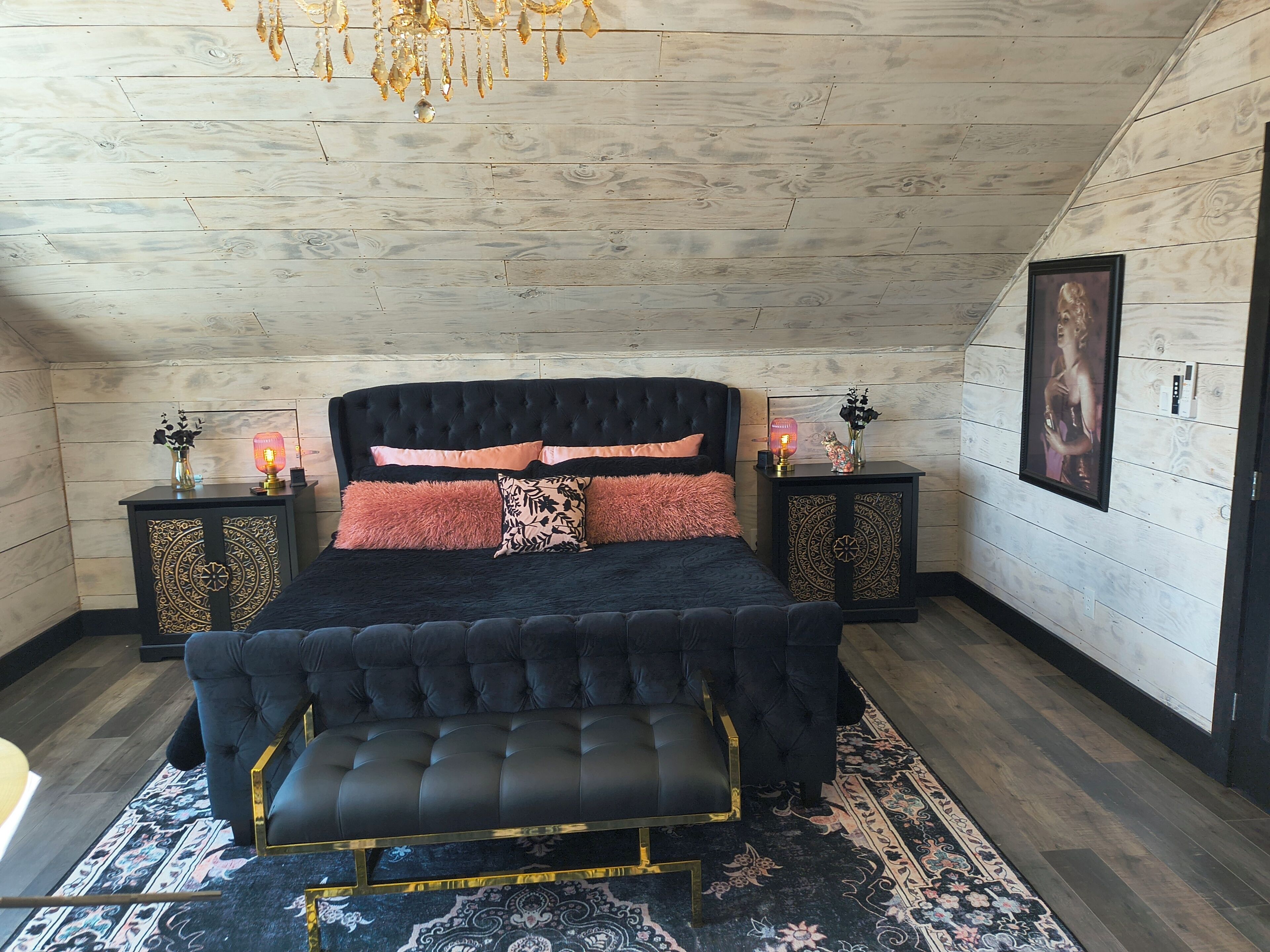 A bedroom with a tufted headboard, a bench, a patterned rug, and two bedside tables with decorative items.