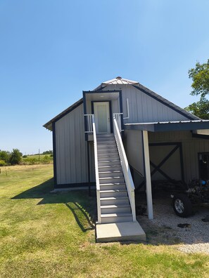 A single-story building with a front door, a staircase leading to a covered porch, and a vehicle parked in the background.