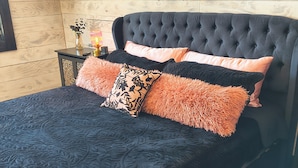 Una cama con cabecera capitonada, edredón acolchado oscuro y varias almohadas de textura mullida.