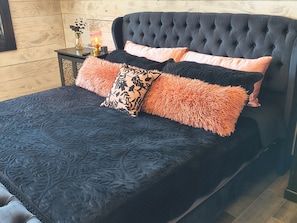 A bed with a tufted headboard, a dark quilted bedspread, and multiple pillows with a fluffy texture.
