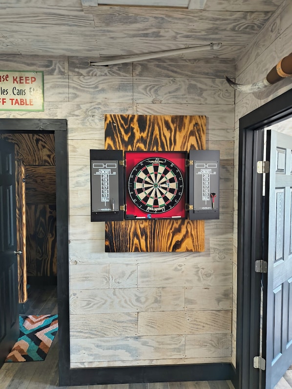 A dartboard mounted on a wall with a wooden pattern, a sign above it, and a door to the left.