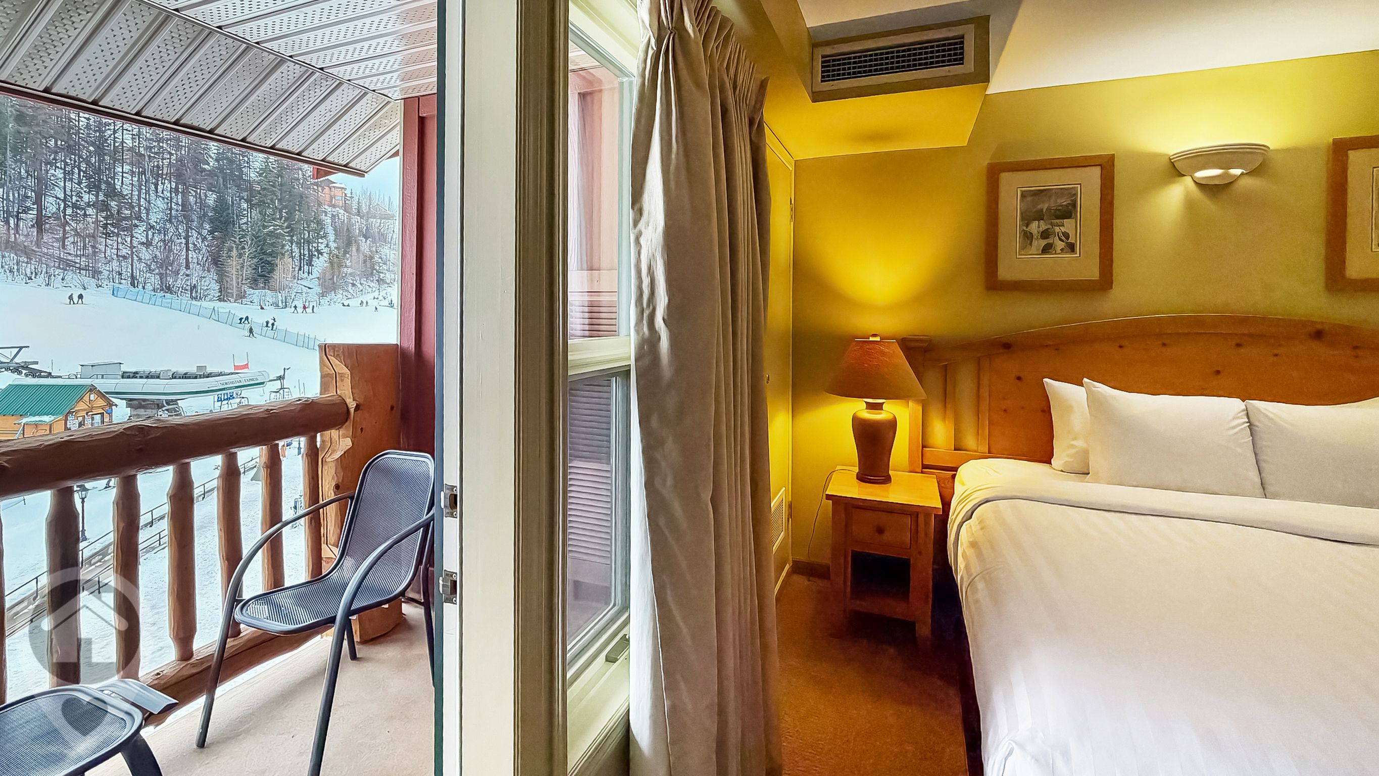 Une chambre d’hôtel avec un lit, une table de chevet avec une lampe, une chaise près de la fenêtre et une vue sur un paysage enneigé avec un télésiège.