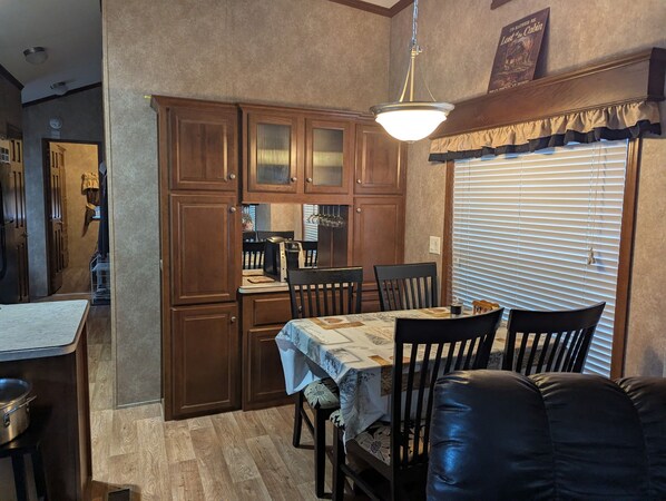 A dining area with a table set for four, wooden cabinets, a chandelier, and a window with blinds.