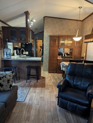 A modern kitchen with wooden cabinets, a dining area with a table and chairs, and a leather sofa in a living room.