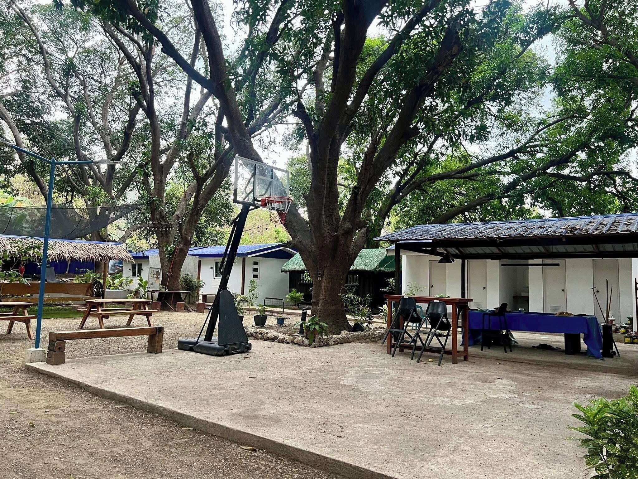 Ett utomhusområde med en basketkorg, picknickbord och en överbyggd sittplats.