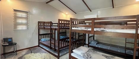 A dormitory room with bunk beds, a small table, and a window with blinds.