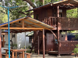 Una cabana de fusta amb un balcó, un porxo cobert i una escala que condueix a un nivell superior.