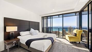 Ein modernes Hotelzimmer mit einem großen Bett, einem Nachttisch, einer Lampe, einem Sessel und einem Balkon mit Blick auf das Meer und die Stadt.