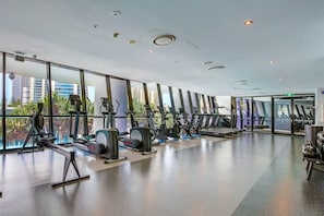 Ein modernes Fitnessstudio mit Laufbändern, einer Hantelbank und großen Fenstern mit Blick auf die Stadt.