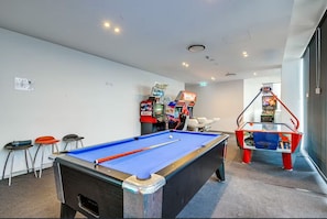 Ein Billardtisch in einem Raum mit Spielautomaten und einem weiteren Billardtisch im Hintergrund.