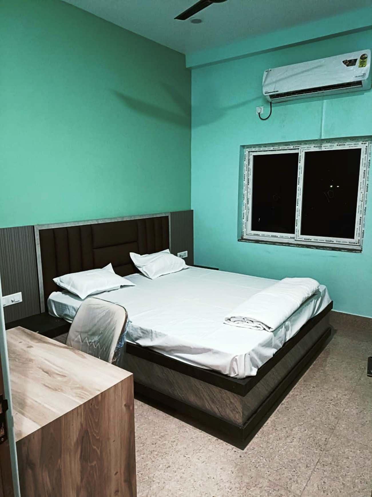 Una cama individual con cabecera, una ventana con persianas bajadas y un equipo de aire acondicionado en la pared.