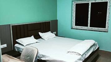 Una cama individual con cabecera, una ventana con persianas bajadas y un equipo de aire acondicionado en la pared.
