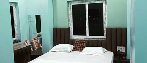 A room with a bed, a window, a bedside table, and an air conditioning unit.