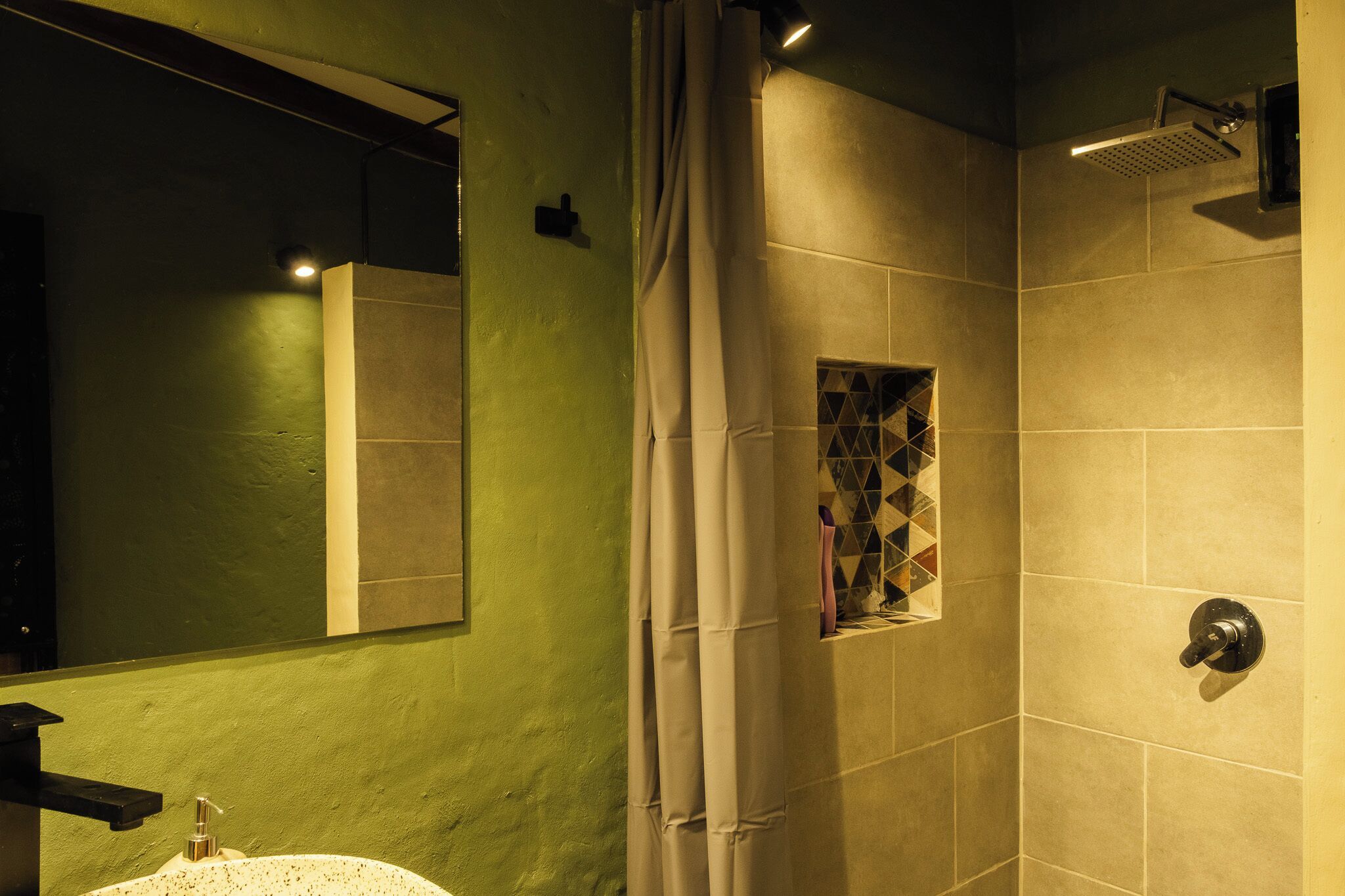 Un baño con pared verde, un espejo, ducha con puerta de cristal y lavabo.