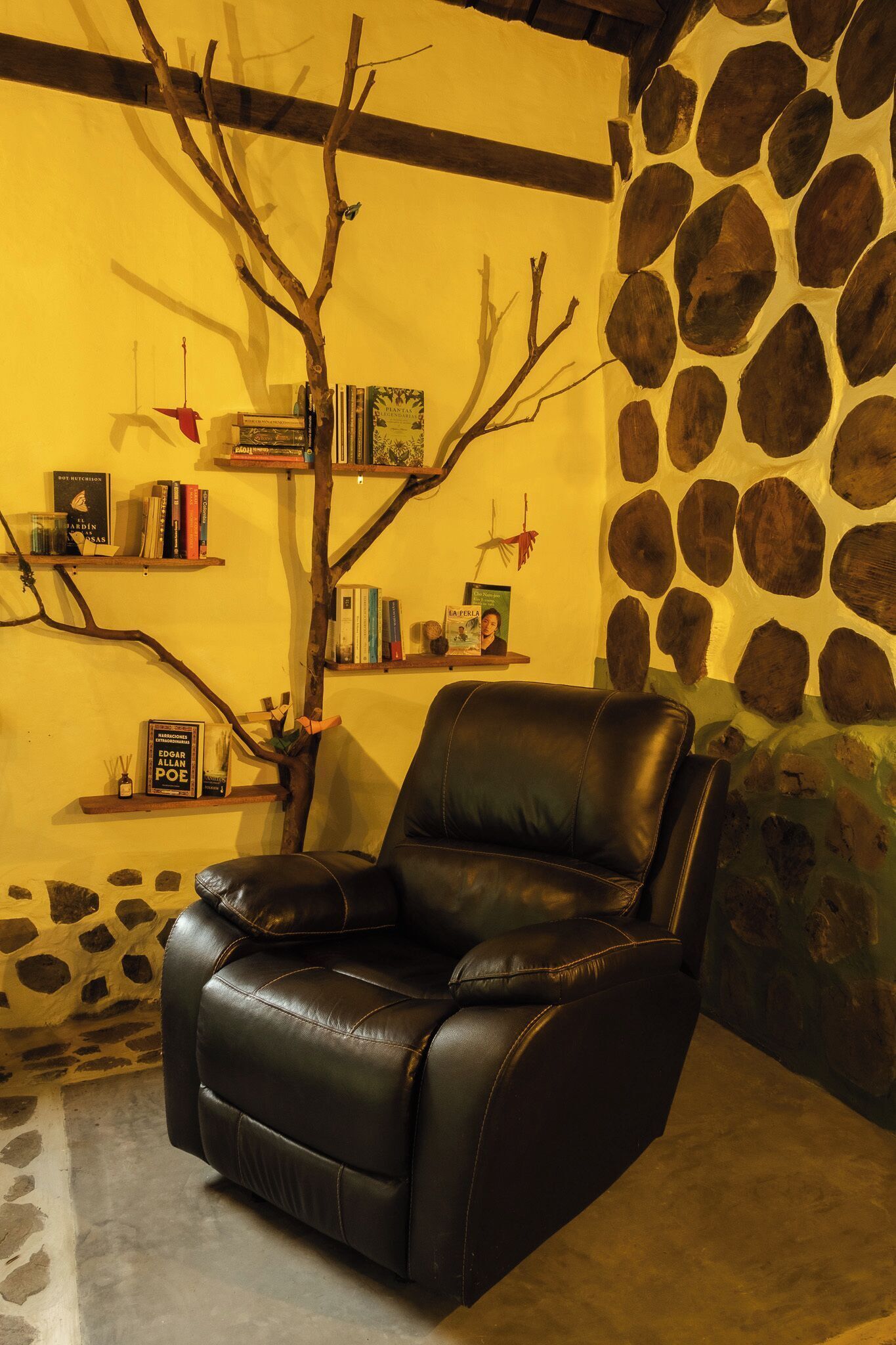 Una silla de cuero negro en una habitación con pared de piedra y estantería.