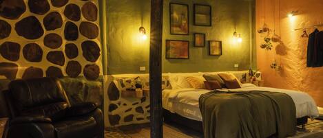 A cozy bedroom with a stone wall, a bed with pillows, a leather chair, and wall-mounted lights.