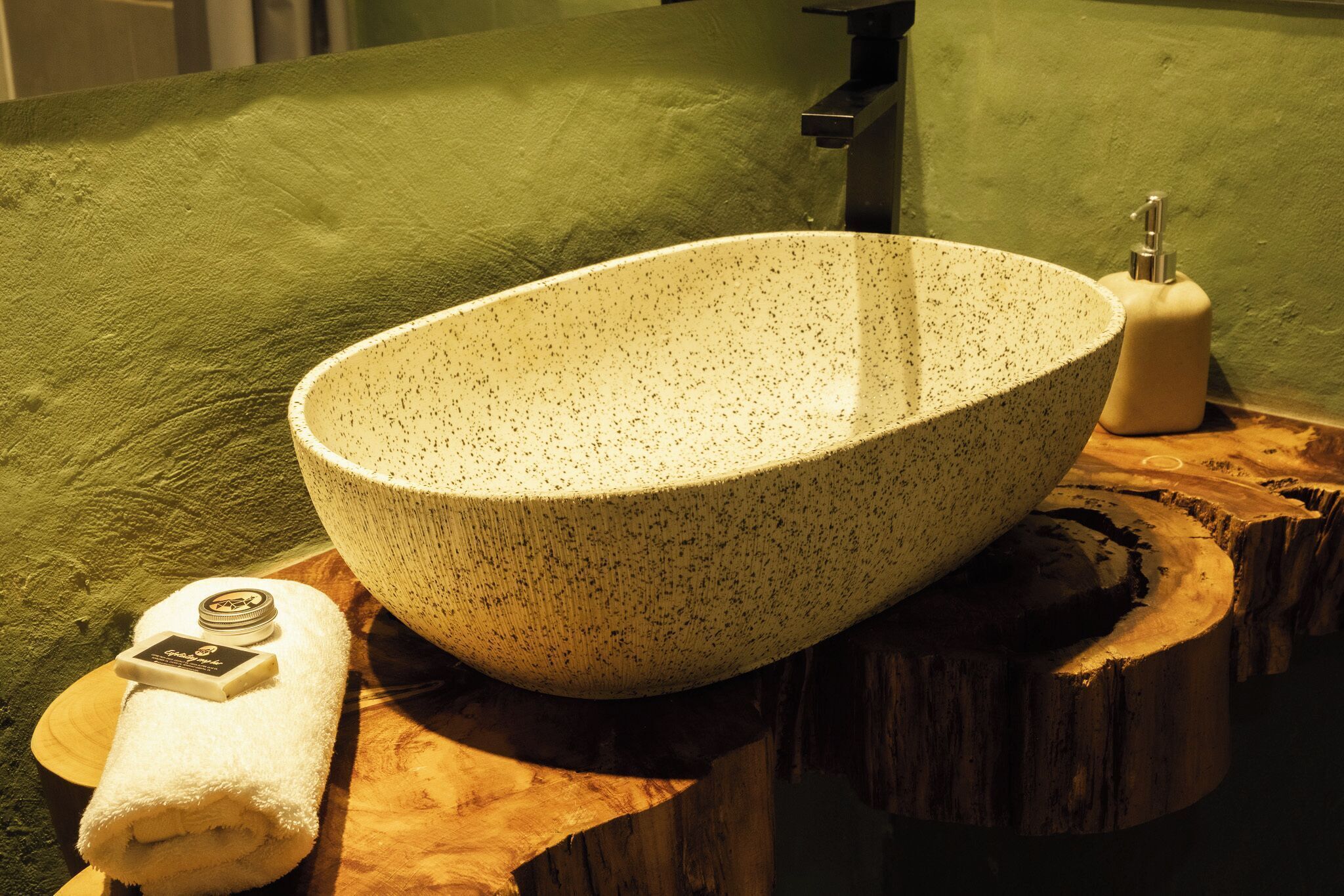 A spa bathroom with a large, speckled basin, a green towel, and a soap dish.