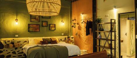 A cozy bedroom with a large woven light fixture, a bed with a green blanket, a brown sofa, and a wooden shelf with books and plants.